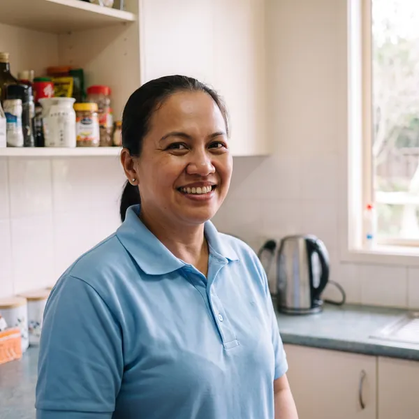 Maricel, smiling, in a light blue polo shirt in a kitchen.