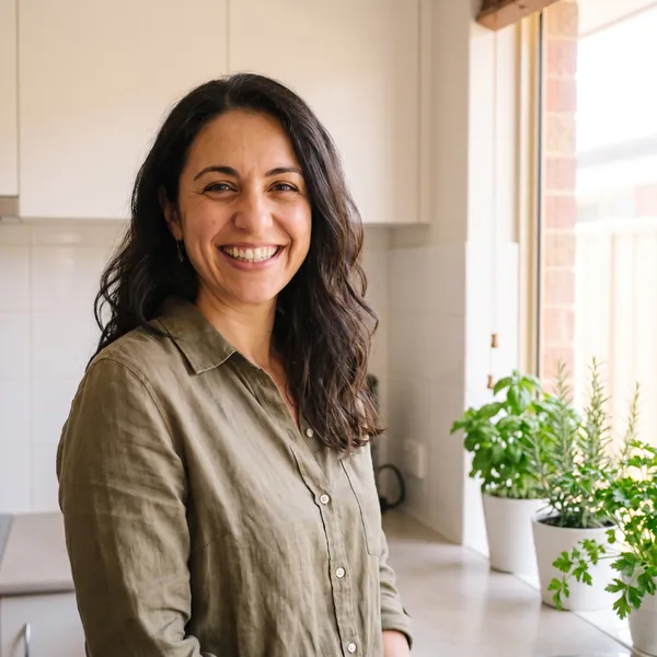 Sara Haddad smiling in a kitchen, pots of herbs on the bench beside her.