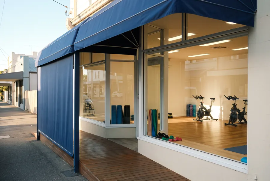 The clinic: a converted shopfront with a deep blue awning and big windows onto the exercise room, bikes and mats inside.