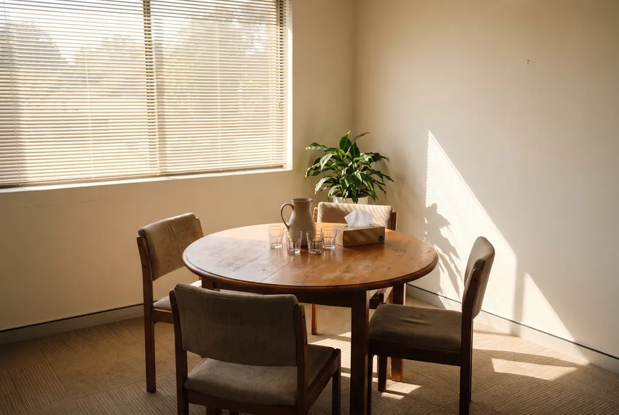 A small meeting room with a round table, three chairs, a water jug and a box of tissues