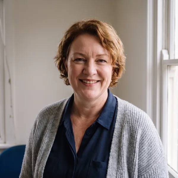 Imogen Voss, smiling, in a grey jumper in front of a sandstone wall at the Murray Street office.