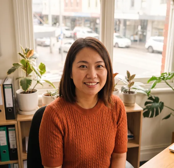 Linh Pham in a rust-coloured jumper, at her desk by the office window