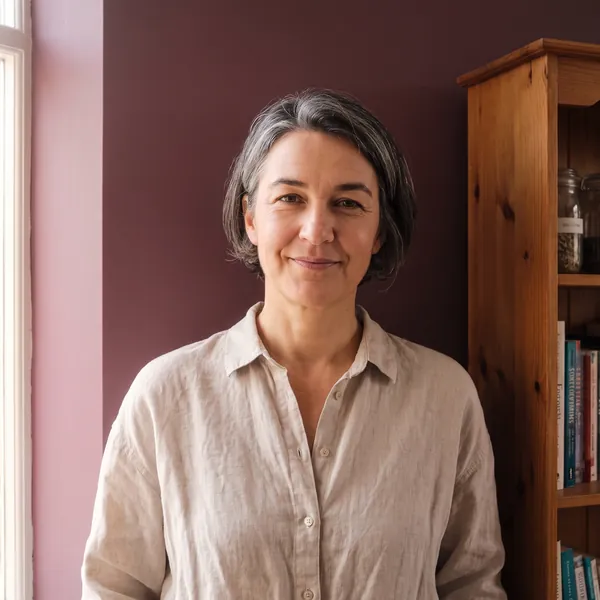 Alex Rowan in a linen shirt, standing by the bookshelf in the consulting room