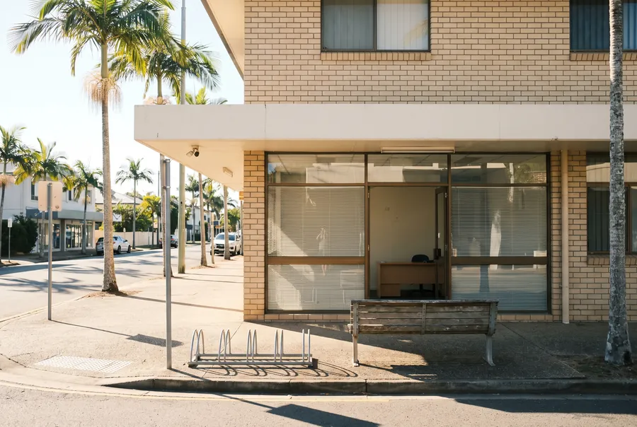 The Mallowbend office: a ground-floor shopfront with a bench outside, on a palm-lined corner of Ocean Street