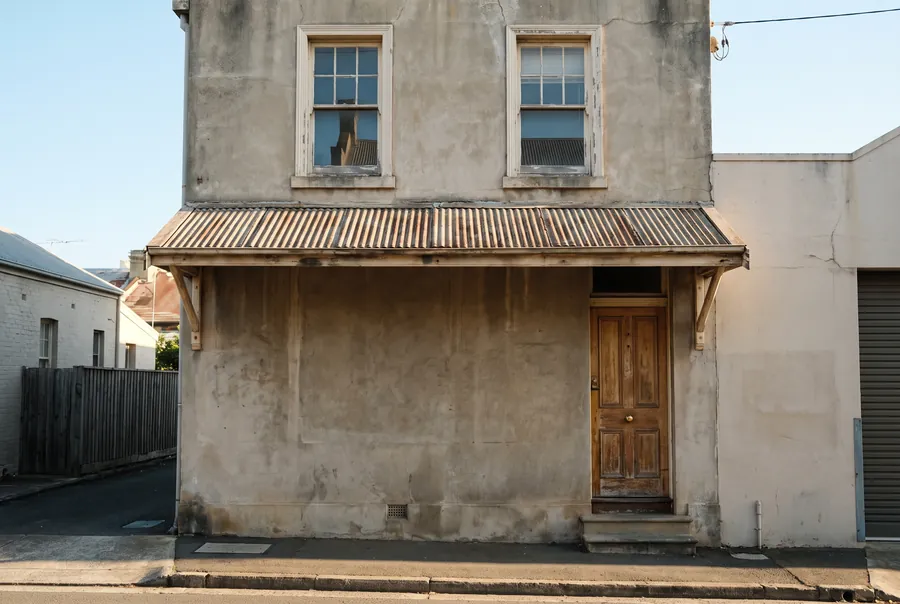 A two-storey rendered building on Hunter Street with a rusty corrugated iron awning and a timber front door, in late afternoon sun.