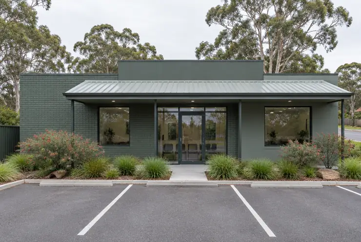 A single-storey green clinic building with marked parking spaces in front